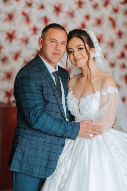 Bir adam ve bir kadın resim için poz veriyorlar. Adam mavi bir takım elbise giyiyor ve kadın beyaz bir elbise giyiyor. İkisi de gülümsüyor ve mutlu görünüyorlar.