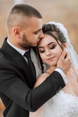 Bir erkek ve bir kadın birbirlerine sarılıyorlar. Adam siyah bir takım elbise ve kravat takıyor. Sahne romantik ve sevgi dolu.