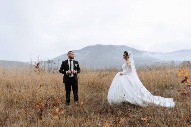 Bir gelin ve damat uzun otların arasında duruyor. Gelin beyaz bir elbise giyiyor ve damat bir takım elbise giyiyor. Sahne dağların arkasına kurulur, huzur yaratır.