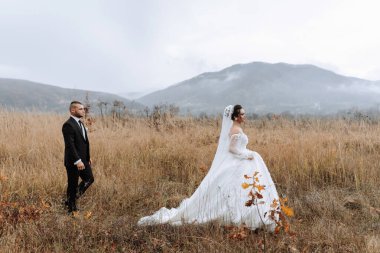 Bir gelin ve damat uzun otların arasında yürüyorlar. Gelin uzun beyaz bir elbise ve duvak takıyor. Adam takım elbise giyiyor. Huzurlu ve huzurlu bir sahne.