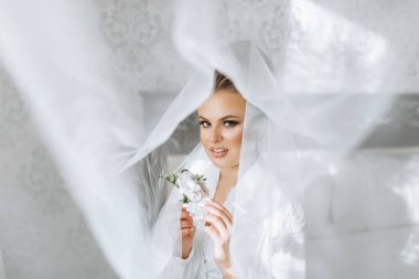 Bir gelin, saçında çiçekle bir resim için poz veriyor. Gelinin beyaz elbisesi ve duvağı sahnenin zarafetini artırıyor.