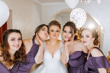 Bir gelin ve nedimeleri balonlu bir resim için poz veriyorlar. Gelin beyaz bir elbise giyiyor ve nedimeler mor elbiseler giyiyor. Sahne neşeli ve kutlayıcıdır.