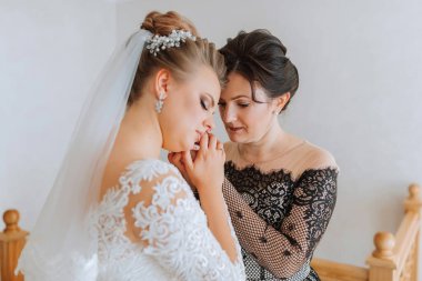 Bir gelin annesi tarafından teselli ediliyor. Gelin beyaz bir elbise ve duvak takıyor. Anne gelinin elini tutuyor.