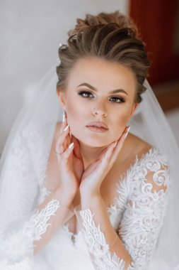 Uzun saçlı ve beyaz gelinlikli bir kadın resim için poz veriyor. O, parmağında bir yüzük takıyor ve ellerini birbirine kenetliyor. Zarafet ve incelik kavramı