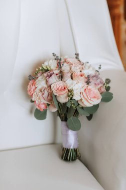 Beyaz bir sandalyede bir buket çiçek duruyor. Çiçekler pembe ve beyaz, ve onları vazoda gibi gösterecek şekilde düzenlenmiş.