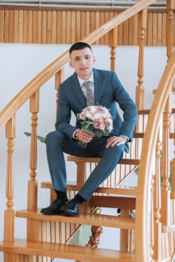 Takım elbiseli bir adam merdivende elinde bir buket çiçekle oturuyor. Zarafet ve incelik kavramı, adam resmi bir takım elbise giymiş ve elinde güzel bir buket çiçek tutuyor.