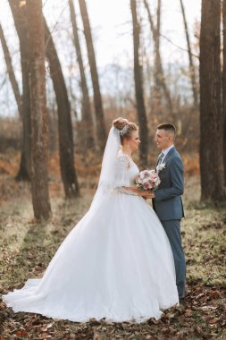 Bir gelin ve damat ağaçlar ve yapraklarla çevrili bir ormanda duruyor. Gelin beyaz bir elbise giyiyor ve damat mavi bir takım elbise giyiyor. El ele tutuşup gülümsüyorlar, mutlu görünüyorlar.