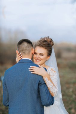 Bir gelin ve damat tarlada birbirlerine sarılıyorlar. Gelin beyaz bir peçe takıyor ve damat mavi bir takım elbise giyiyor. Sahne mutlu ve neşeli.