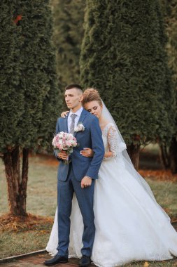 Gelin ve damat bir ağacın önünde, gelin bir buket tutuyor.