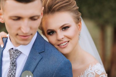 Gelin ve damat fotoğraf için poz veriyor, gelin gülümsüyor ve damat ona bakıyor.