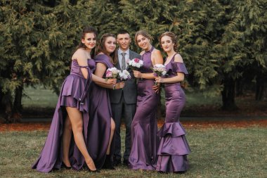 Mor elbiseli bir grup kadın fotoğraf için poz veriyor. Ortadaki adam bir takım elbise giyiyor. Sahne zarif ve resmi.