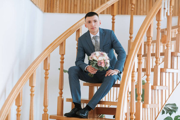 A man in a suit is sitting on a staircase holding a bouquet of flowers. Concept of elegance and sophistication, as the man is dressed in a formal suit and holding a beautiful bouquet of flowers
