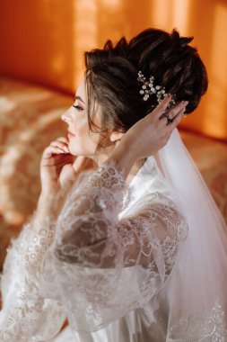 Kafasında duvak olan beyaz elbiseli bir kadın. Kolye ve yüzük takıyor.