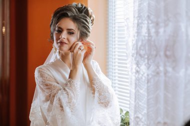 Bir kadın düğün için hazırlanıyor ve gelinliğini giyiyor. Aynada kendine bakıyor ve elbisesini düzeltiyor.