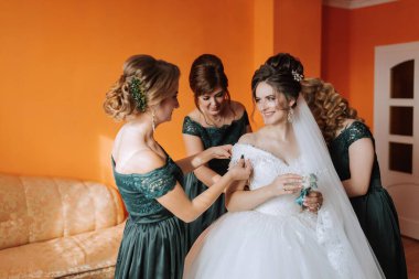 Bir gelin nedimeleriyle düğününe hazırlanıyor. Gelin beyaz bir elbise giyiyor ve nedimeler yeşil elbiseler giyiyor. Hepsi gülümsüyor ve mutlu görünüyorlar.