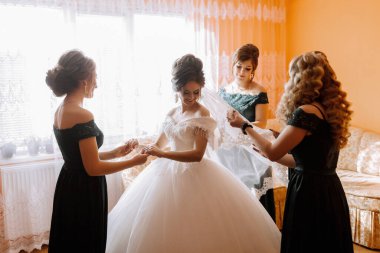 Dört kadın düğün için hazırlanıyor. Bir tanesi bir geline peçe takıyor.