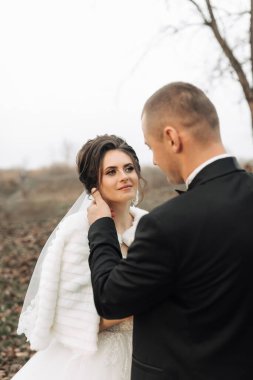 Gelin ve damat tarlada duruyorlar, gelin beyaz kürk manto giyiyor. Damat gelinin boynuna dokunuyor.