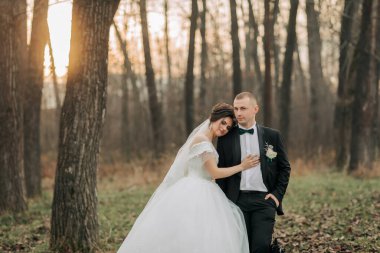 Gelin ve damat ormanda oturuyor, gelin beyaz bir elbise ve damat siyah bir takım elbise giyiyor.