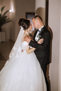 Bir gelin ve damat bir düğün töreninde birbirlerini kucaklıyorlar. Gelin beyaz bir elbise giyiyor ve damat siyah bir takım elbise giyiyor. Sahne aşk ve mutluluktur.