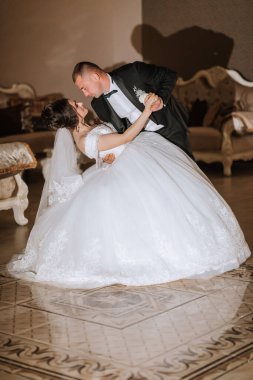 Bir gelin ve damat bir balo salonunda dans ediyorlar. Gelin beyaz bir elbise giyiyor ve damat siyah bir takım elbise giyiyor. Çift düğünlerini kutlarken sahne romantik ve neşeli.