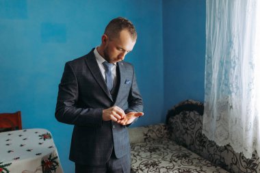 Takım elbiseli bir adam dışarı çıkmaya hazırlanıyor. Kravat takıyor ve saatini kontrol ediyor.