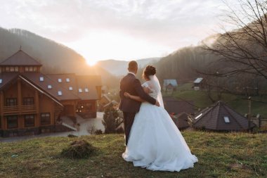 Bir gelin ve damat bir evin önündeki çimenli bir yamaçta dururlar. Güneş batıyor, sahne üzerine sıcak bir parıltı saçıyor. Çift resmi giyinmiş.