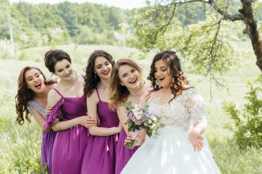 Bir grup kadın tarlada fotoğraf çektirmek için poz veriyor. Kadınlardan biri elinde bir buket çiçek tutuyor.