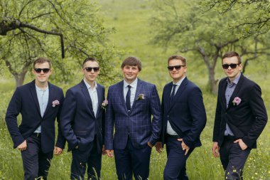 Takım elbiseli ve güneş gözlüklü beş kişilik bir grup bir tarlada duruyor. Hepsi gülümsüyor ve poz veriyor.