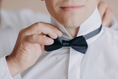 Bir adam siyah bir papyon takmaya hazırlanıyor. Ayarlıyor ve düzgün bağlandığından emin oluyor.