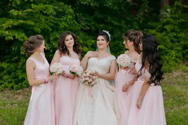 Bir grup kadın bir fotoğraf için poz veriyor, içlerinden biri gelinlik giyiyor. Kadınların hepsi pembe elbiseler giyiyor ve kameraya gülümsüyorlar.