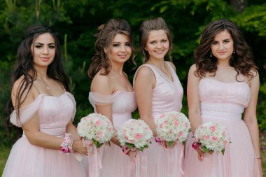 Pembe elbiseli dört kadın ellerinde çiçek buketleri tutuyor. Sahne neşeli ve kutlama dolu.