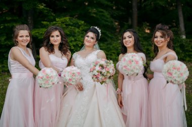 Bir grup kadın fotoğraf için poz veriyor, içlerinden biri gelinlik giyiyor. Buketleri tutuyorlar ve kameraya gülümsüyorlar.