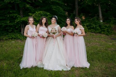 Pembe elbiseli bir grup kadın fotoğraf için poz veriyor. Gelin, grubun merkezinde, arkasında duran diğer kadınlarla birlikte duruyor. Sahne neşeli ve kutlayıcıdır.