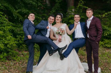 Bir grup erkek ve bir kadın resim için poz veriyor. Soldaki adam mavi bir takım elbise giyiyor ve kadın beyaz bir elbise giyiyor.