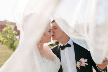 Bir gelin ve damat peçenin altında öpüşüyor. Gelin beyaz bir elbise giyiyor ve damat siyah bir takım elbise giyiyor. Sahne samimi ve romantik, aşkı yakalıyor.