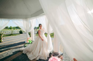 Beyaz elbiseli bir kadın beyaz bir çadırın önünde duruyor. Sahnenin romantik bir tarafı var.