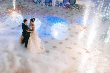 Bir gelin ve damat bir balo salonunda dumanla ve ateşle dans ediyor. Sahne romantik ve kutlayıcıdır.