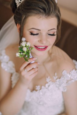 Bir gelin elinde bir çiçek tutuyor, yüzünde bir gülümsemeyle. Çiçek beyazdır ve küçük mor bir merkezi vardır. Gelin beyaz bir elbise ve duvak takıyor.