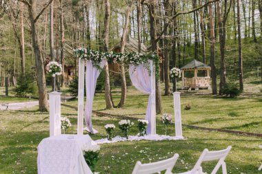Beyaz kemerli ve beyaz çiçekli bir parkta bir düğün töreni düzenleniyor. Tören, yakınlarda bir taraça bulunan bir ormanda yapılacak. Sandalyeler kemerin etrafına dizildi.