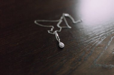 Tahta bir masada üzerinde elmas kolye olan bir kolye duruyor. Kolye gümüşten ve ortasında bir elmas var. Masa koyu kahverengi ve üzerindeki tek şey kolye.