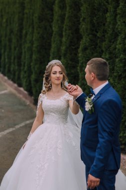 Bir gelin ve damat bir çitin önünde duruyor. Gelin beyaz bir elbise giyiyor ve damat mavi bir takım giyiyor.