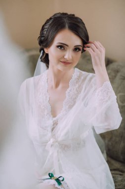 Beyaz cüppeli bir kadın kanepede oturuyor. Duvak takmış ve saçları topuz gibi olmuş.