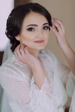 Bir kadın beyaz bir elbise giyiyor ve saçlarına dokunuyor. Parmağında bir yüzük var ve gülümsüyor.