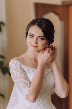 Bir kadın kulaklarını deldiriyor. O beyaz bir elbise giyiyor ve gülümsüyor. Mutluluk ve kutlama kavramı