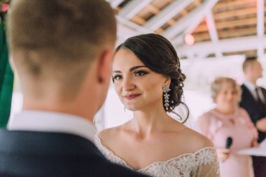 Bir gelin ve damat düğün töreninde birbirlerine bakıyorlar. Gelin beyaz bir elbise giyiyor ve damat mavi bir takım elbise giyiyor. Sahne aşktır.