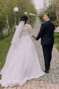 Bir gelin ve damat bahçede bir patikada yürüyorlar. Damat takım elbise giyerken gelin beyaz bir elbise ve peçe takıyor. El ele tutuşuyorlar ve mutlu ve aşık görünüyorlar.