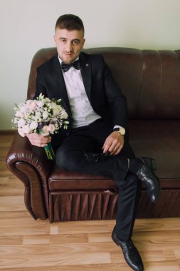 Takım elbiseli ve papyonlu bir adam elinde bir buket çiçekle kanepede oturur. Zarafet ve entelektüellik anlayışı, çünkü adam resmi giyinmiş.