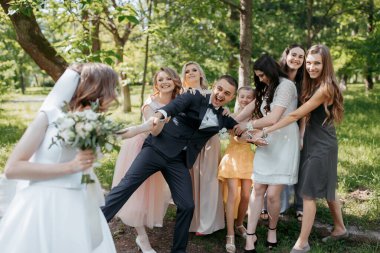 Gelin ve damadın etrafı düğün partileriyle çevrili. Gelin de elinde buket tutuyor. Sahne neşeli ve kutlayıcıdır.