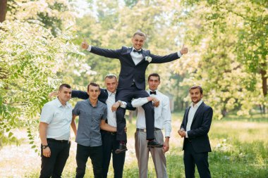 Bir grup adam fotoğraf için poz veriyor, bir adam diğerlerinin omuzlarında duruyor. Sahne neşeli ve eğlenceli, çünkü erkekler birbirlerinin arkadaşlığından zevk alıyor ve iyi vakit geçiriyorlar.