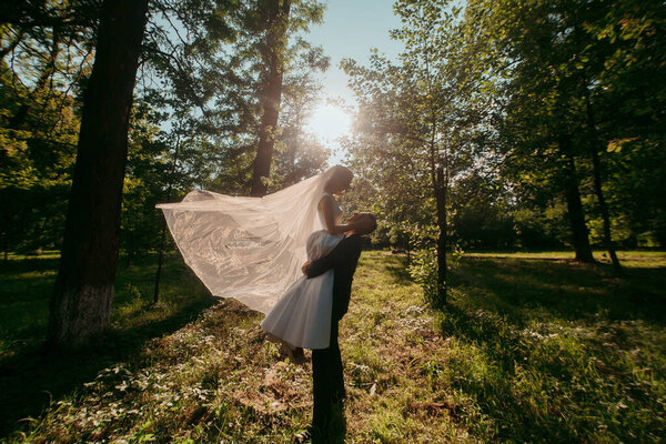 A bride and groom are standing in a field with the bride holding a veil over the groom's head